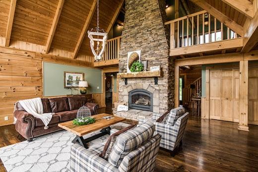 Photo of great room with a-frame ceiling of exposed wood and exposed wood walls. A stone fireplace separates the great room from a family informal space. the chimney provides a partial wall for the second story loft