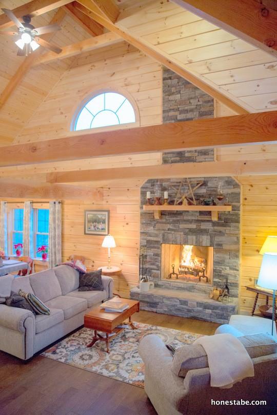 Photo of great room of log home with a-frame exposed beams and soaring a-frame ceiling. The walls are a matching honey oak and the wood floors are a darker wood